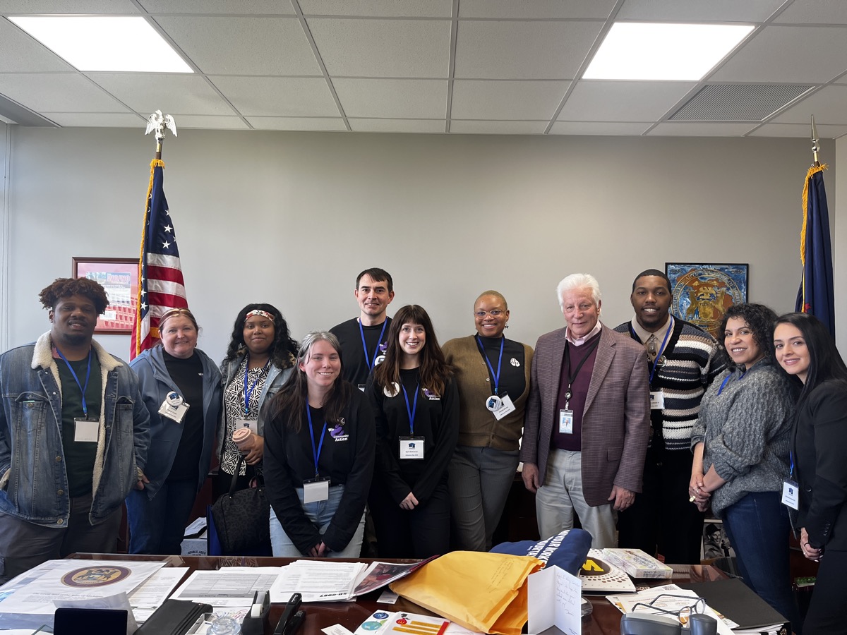 The team poses with staff in a Michigan legislator's office, with US flags displayed in the background